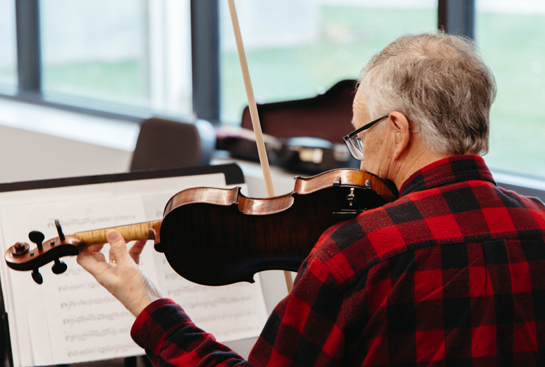 An adult member of the Myelin Ensemble at Omaha Conservatory of Music plays a violin.
