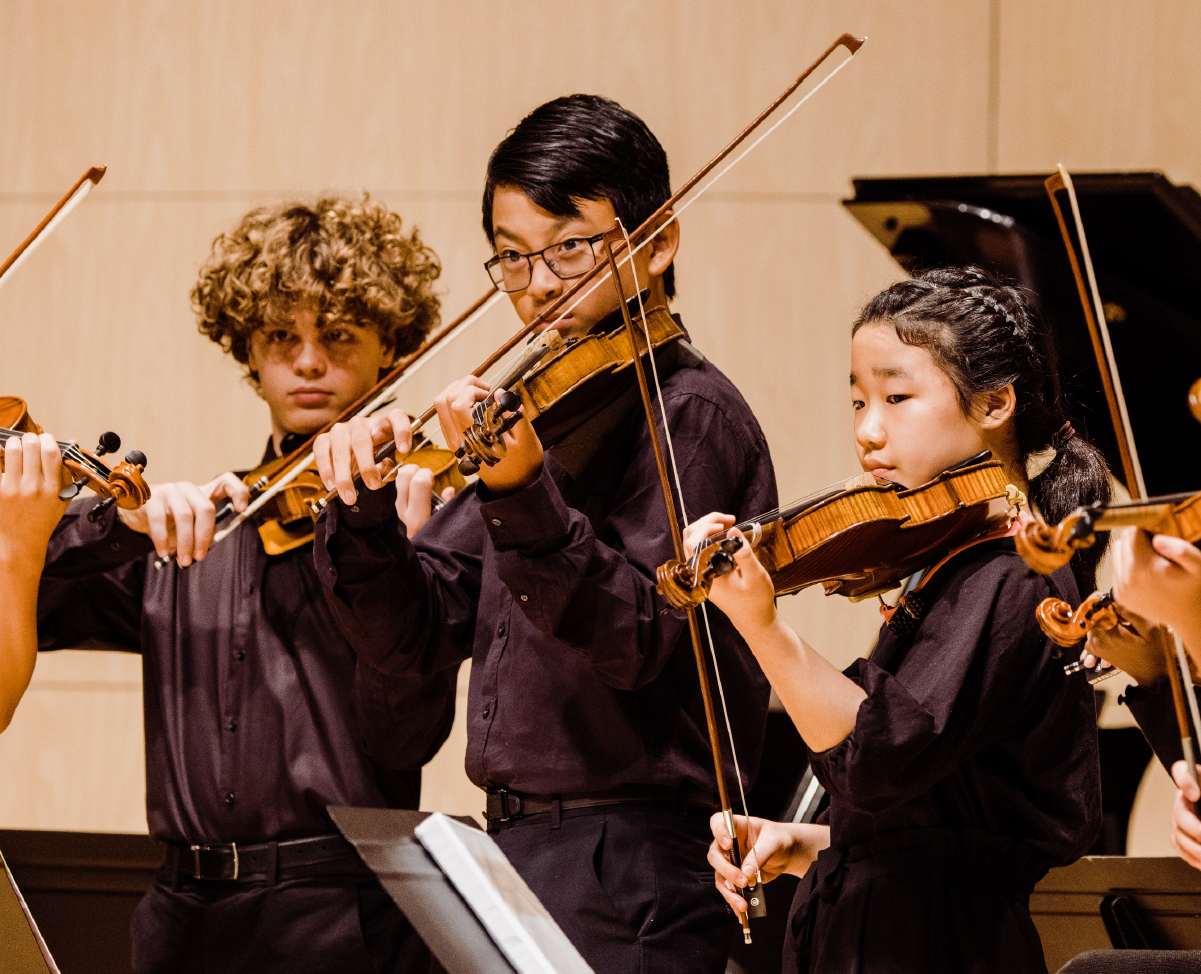 Three violin players perform on stage at the Omaha Conservatory.